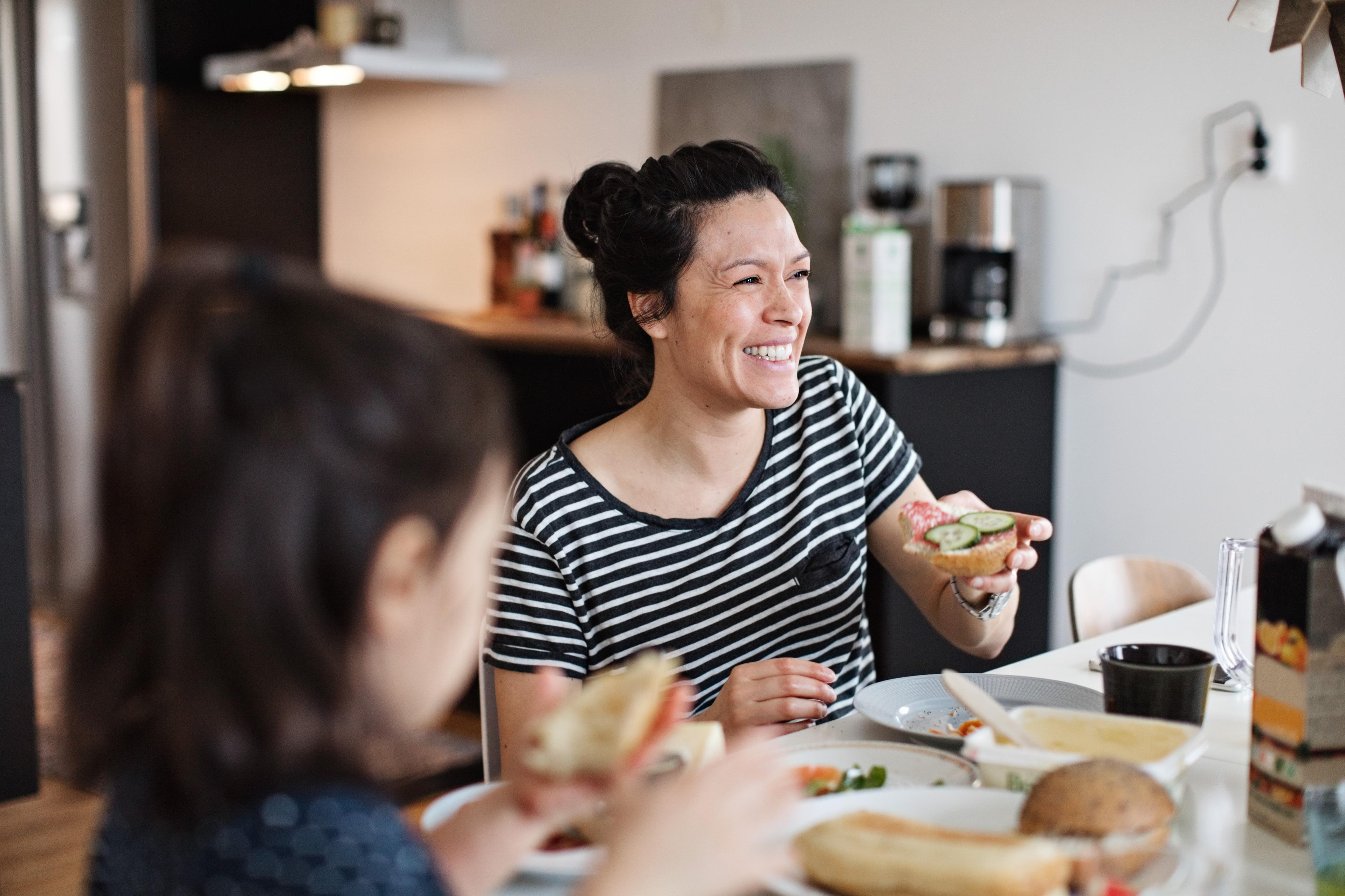 Leende mamma sitter vid köksbordet och äter frukost med sin dotter