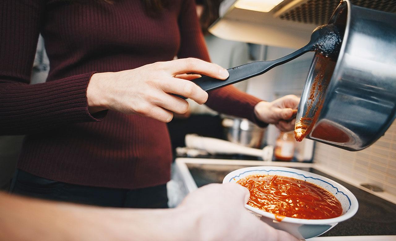 Utsnitt av kvinna som häller upp tomatsoppa i en djup tallrik