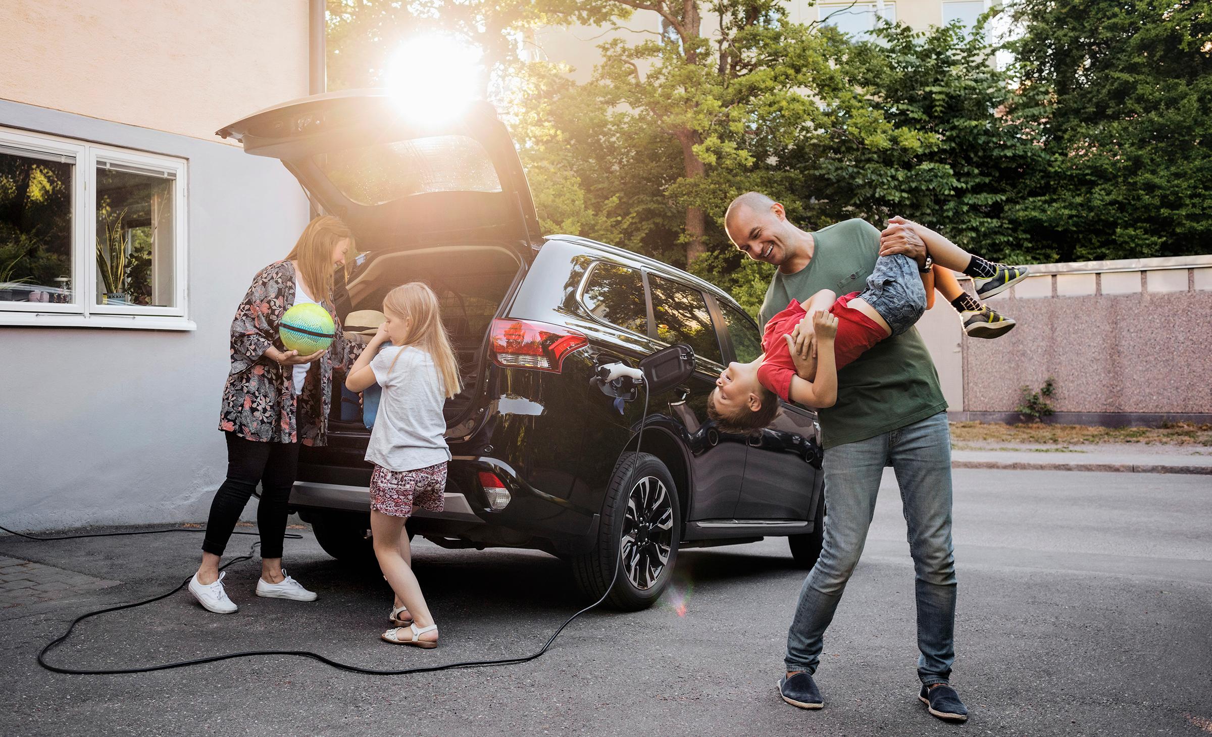 Pappa skojar med son med mamma och dotter som packar bil på uppfart